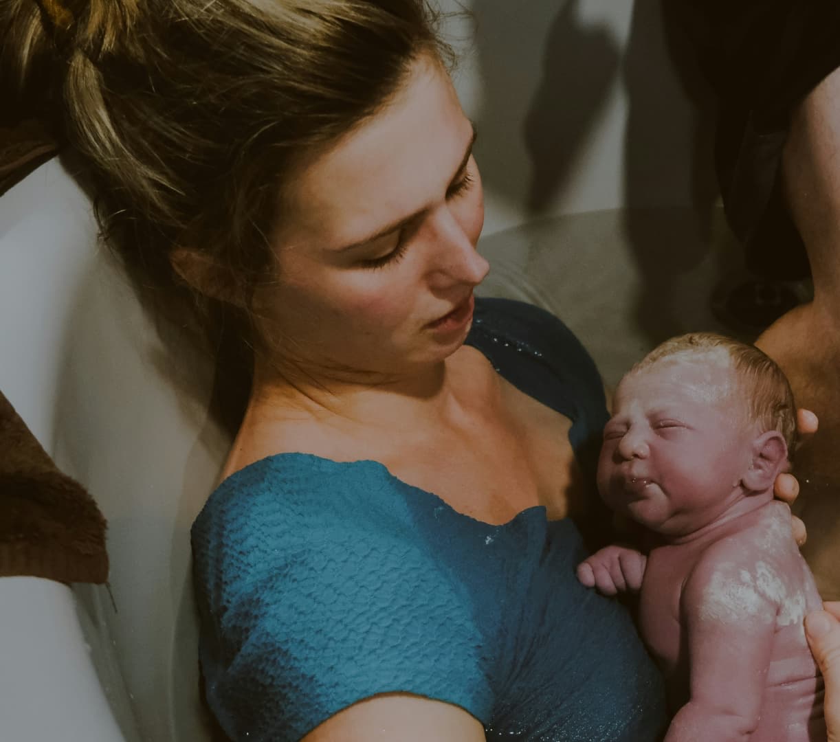 Eine Mutter sitzt in einer Gebärwanne und hält ihr frischgeborenes Baby im Arm.